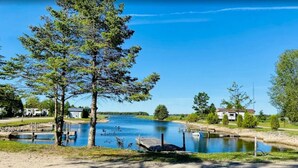 A lakeside view with a dock, trees, and a building in the background. - Fantastic campground retreat #35 (Lion's Head)