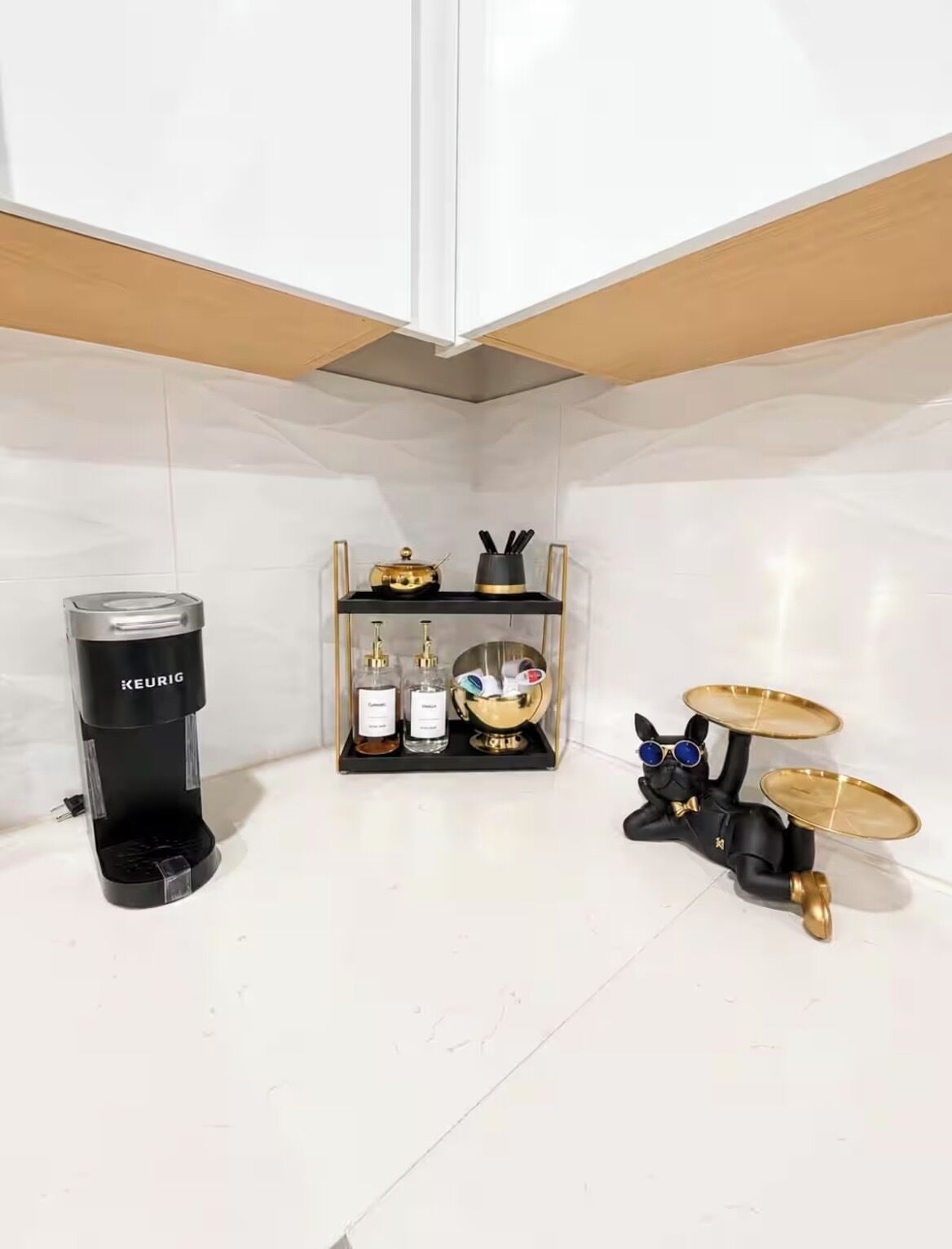 Eine Küchenzeile mit einer Keurig-Kaffeemaschine, einem schwarzen Regal mit Pflegeprodukten und einer schwarzen Katzenfigur, die Schlagzeug spielt.