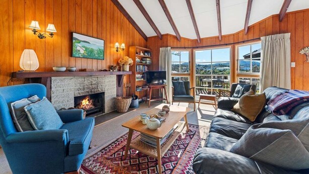 Ein gemütliches Wohnzimmer mit Kamin, Holzwänden, einem großen Fenster mit Aussicht und einem blauen Sessel.
