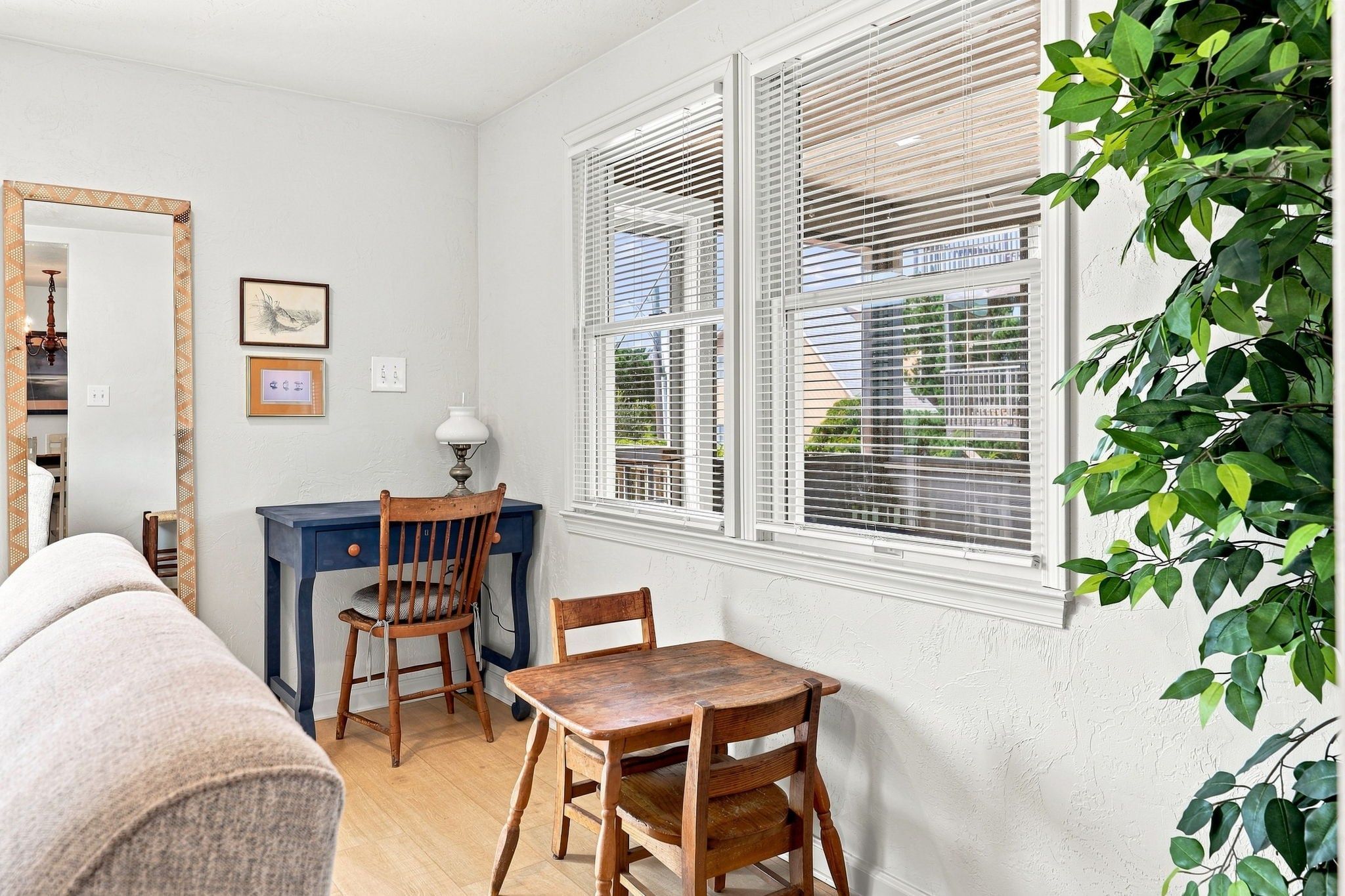 A room with a wooden table and chairs, a blue desk, a mirror, and a window with blinds.