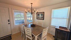 A dining area with a wooden table, white chairs, a chandelier, and a framed picture on the wall. - The Hatch: New to the Program, Close to the Beach, Pet-Friendly (Avon)