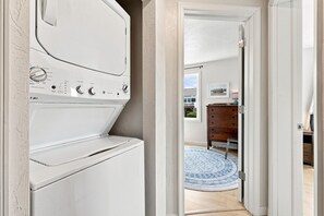 A laundry room with a front-loading washer and dryer, a wooden dresser, and a blue patterned rug in the adjacent hallway. - The Hatch: New to the Program, Close to the Beach, Pet-Friendly (Avon)