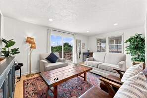 Ein Wohnzimmer mit zwei Sofas, einem Couchtisch, einer Stehlampe und einem großen Fenster mit Jalousien.