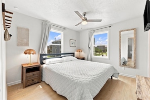 A bedroom with a bed, two bedside lamps, a ceiling fan, a window with curtains, and a wall-mounted mirror. - The Hatch: New to the Program, Close to the Beach, Pet-Friendly (Avon)