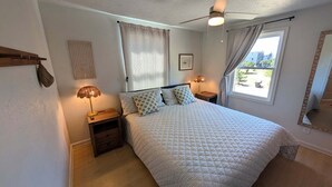 A bedroom with a bed, two bedside lamps, a ceiling fan, and a window with curtains. - The Hatch: New to the Program, Close to the Beach, Pet-Friendly (Avon)