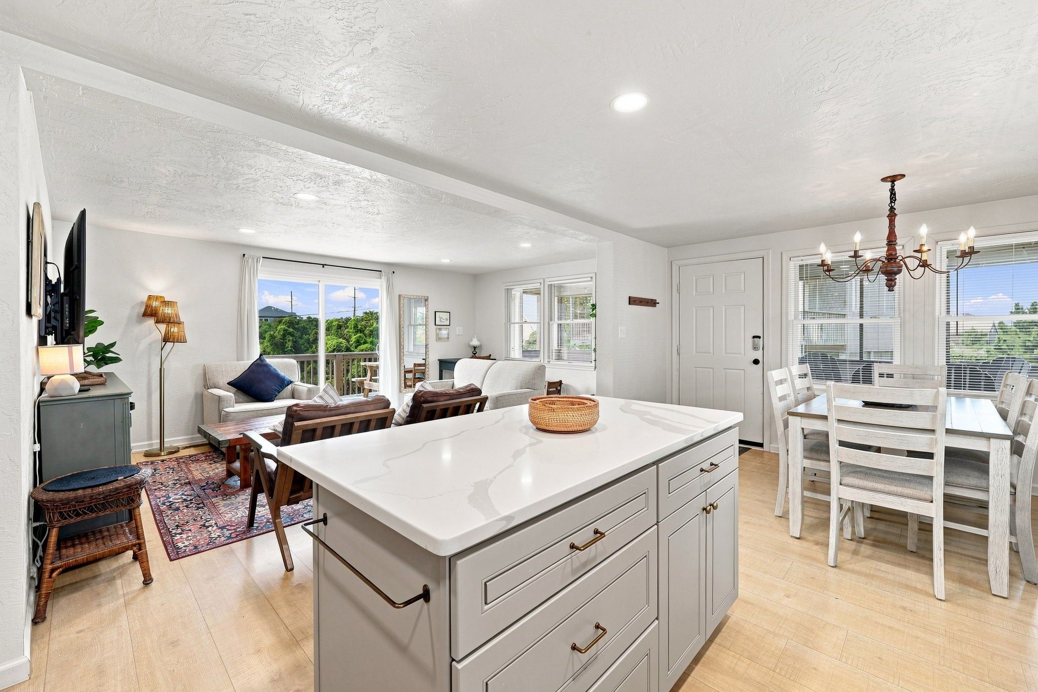 A modern kitchen with a large island, dining area, and a view of greenery outside.