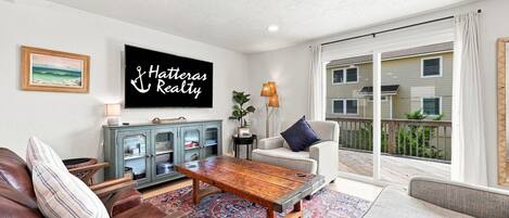 Ein Wohnzimmer mit Fernseher, einer Couch, einem Couchtisch und Blick auf ein Gebäude durch eine Glastür.