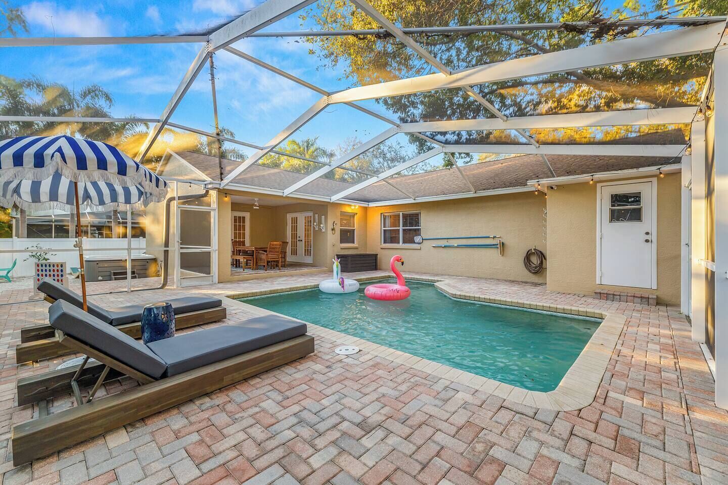 A covered outdoor swimming pool with lounge chairs, a flamingo float, and a patio area with a table and chairs.