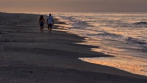 Uma praia ao pôr do sol, com duas pessoas caminhando pela areia.