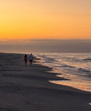 Ein Strandbild mit zwei Personen, die bei Sonnenuntergang am Ufer entlanggehen.