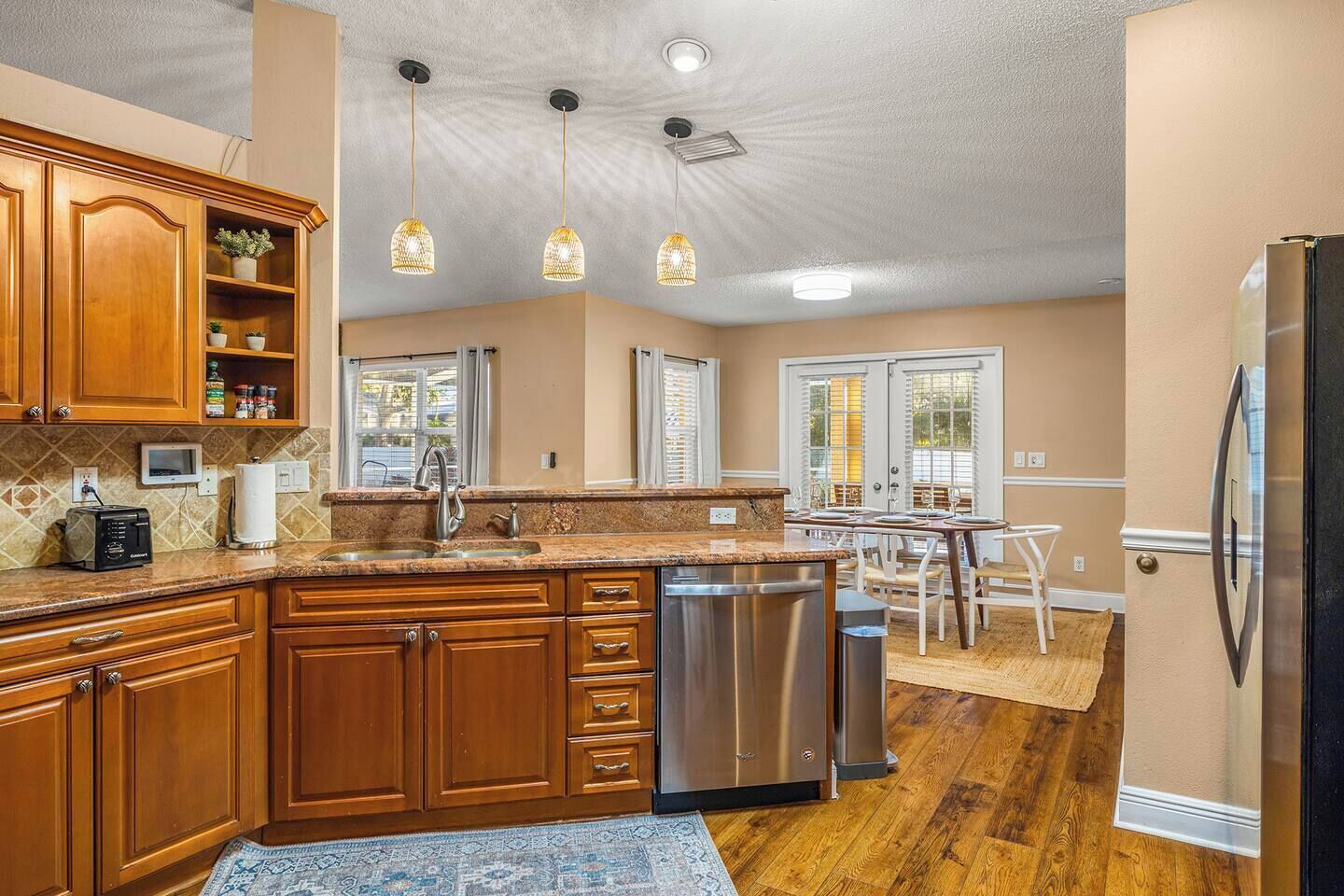 A kitchen with wooden cabinets, a stainless steel dishwasher, and pendant lights.