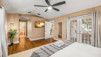 A bedroom with a bed, a ceiling fan, a TV, and a view of the outside.