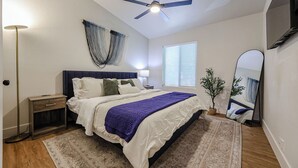 A bedroom with a bed, bedside table, nightstand, ceiling fan, window, and a large mirror. - Olive & Oak Retreat King Bed Pool Fast WiFi (Phoenix)