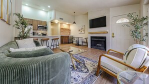 A modern living room with a sofa, a glass coffee table, a fireplace, and a kitchen area with wooden cabinets and a microwave. - Olive & Oak Retreat King Bed Pool Fast WiFi (Phoenix)
