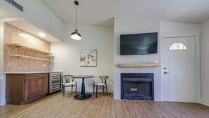 A modern kitchen with wooden cabinets, a dining area with a round table and chairs, a fireplace, and a mounted TV. - Olive & Oak Retreat King Bed Pool Fast WiFi (Phoenix)