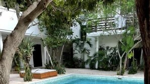 A swimming pool with a tiled deck, surrounded by plants and a white building. - Carmela  (Tulum)