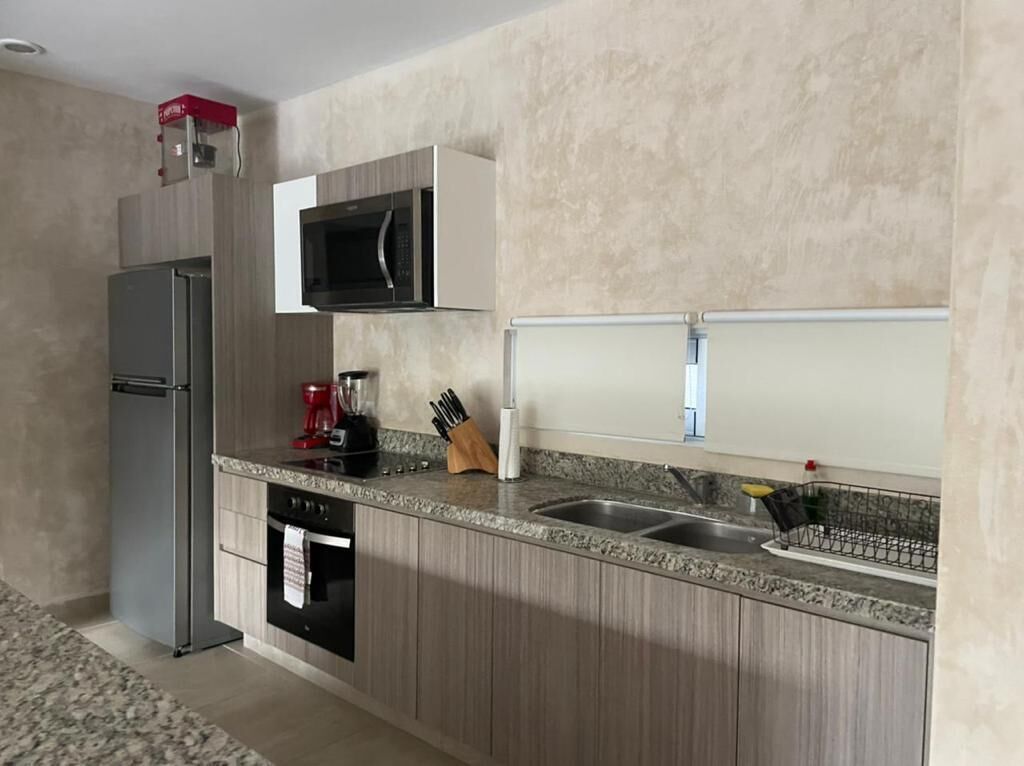 A compact kitchen with a built-in microwave, a stainless steel refrigerator, a coffee maker, and a knife block.