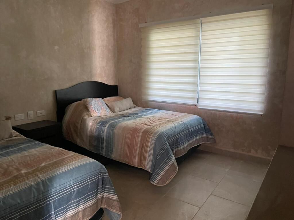 Una camera da letto con due letti, una finestra con persiane e un muro spoglio.