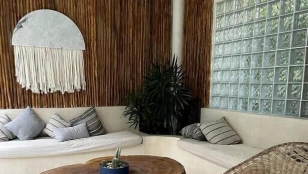 A living room with a round coffee table, a wicker chair, a sofa, and a large window with a grid pattern. - Carmela  (Tulum)