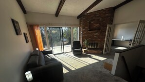 Een woonkamer met een bank, een stoel, een open haard en een schuifpui naar een balkon.