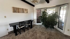 Een kamer met een donker houten tafel en stoelen, een kroonluchter, een groot raam met uitzicht en een kunstwerk aan de muur.