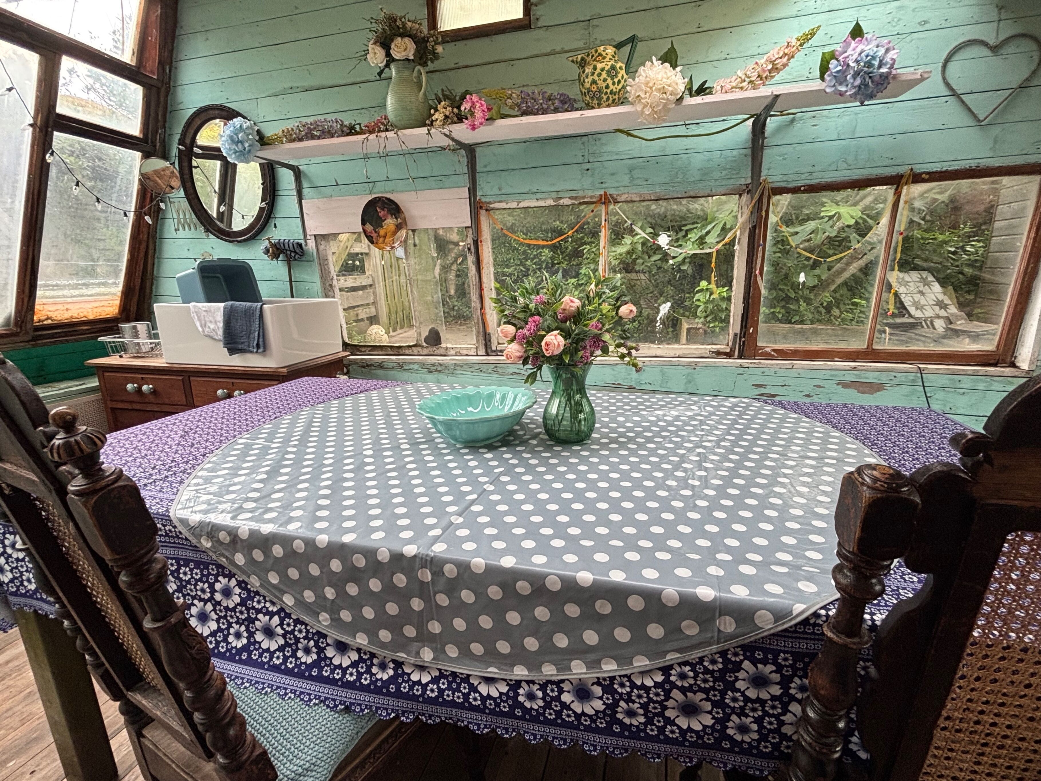 A cozy room with a round table, a chair, a dresser, a mirror, and a window with a view of greenery.