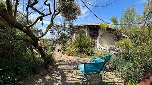 Um jardim com uma cadeira, uma estrutura de concreto e diversas plantas.