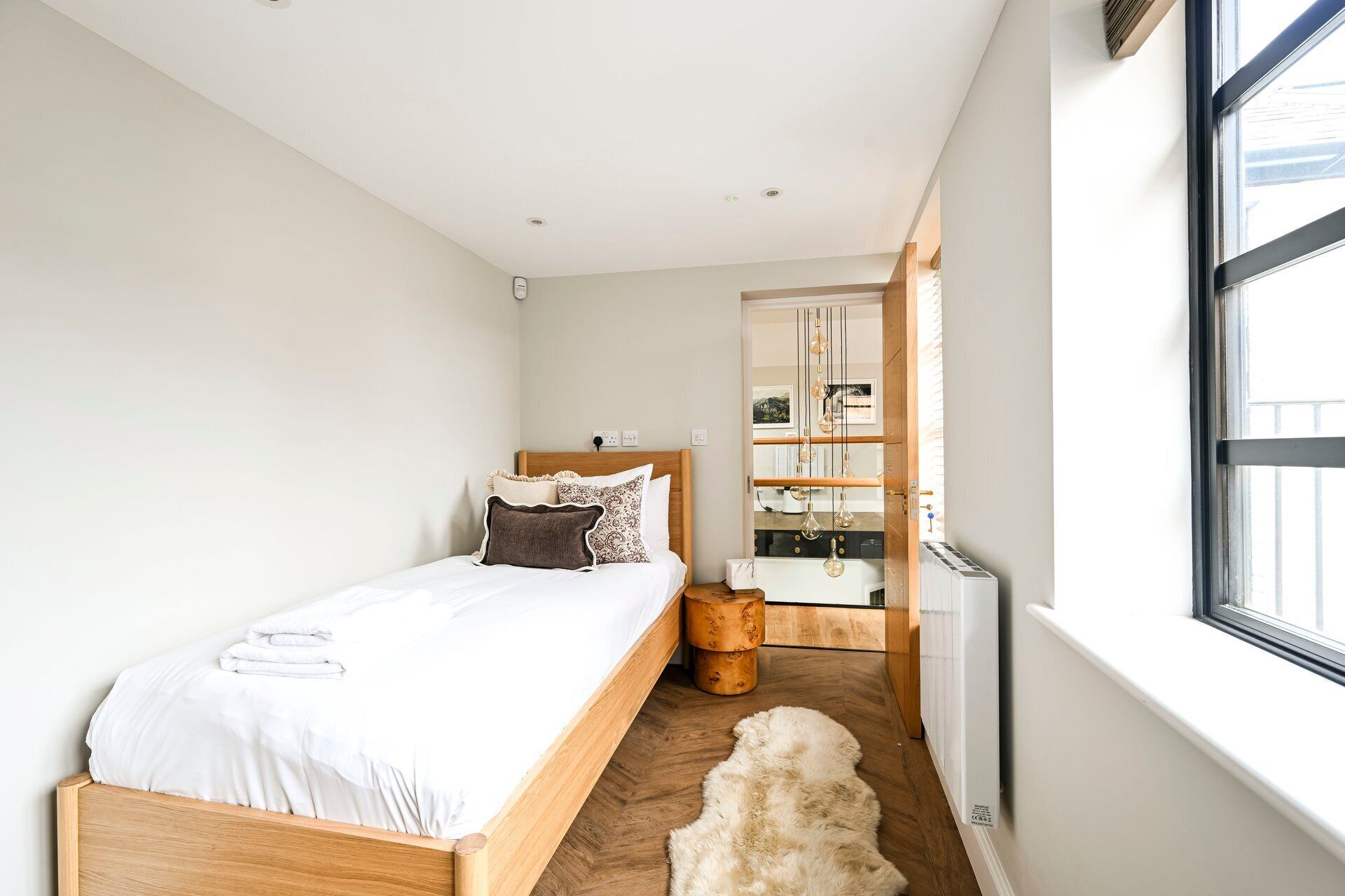 A bedroom with a wooden bed, a white radiator, a fur rug, and a window with blinds.