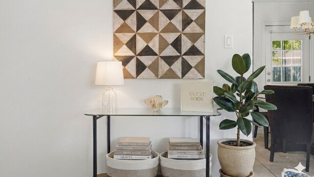 A room with a geometric wall art, a table with a lamp, a guest book, and a potted plant. - 2BR Garden Pool Home❤️ Walk to Barton Springs, Zilker & Dining (Austin)