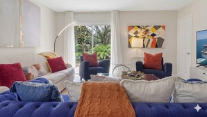 A modern living room with a sofa, armchairs, and a coffee table. There is a painting on the wall and a television on the right. - 2BR Garden Pool Home❤️ Walk to Barton Springs, Zilker & Dining (Austin)