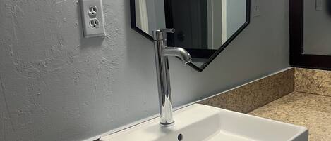 Un baño con un lavamanos blanco, un espejo rectangular y una encimera de granito.