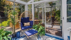A conservatory with a wicker chair, blue cushions, and potted plants. - Bella Azul - Charming Home Minutes from Campus (Eugene)