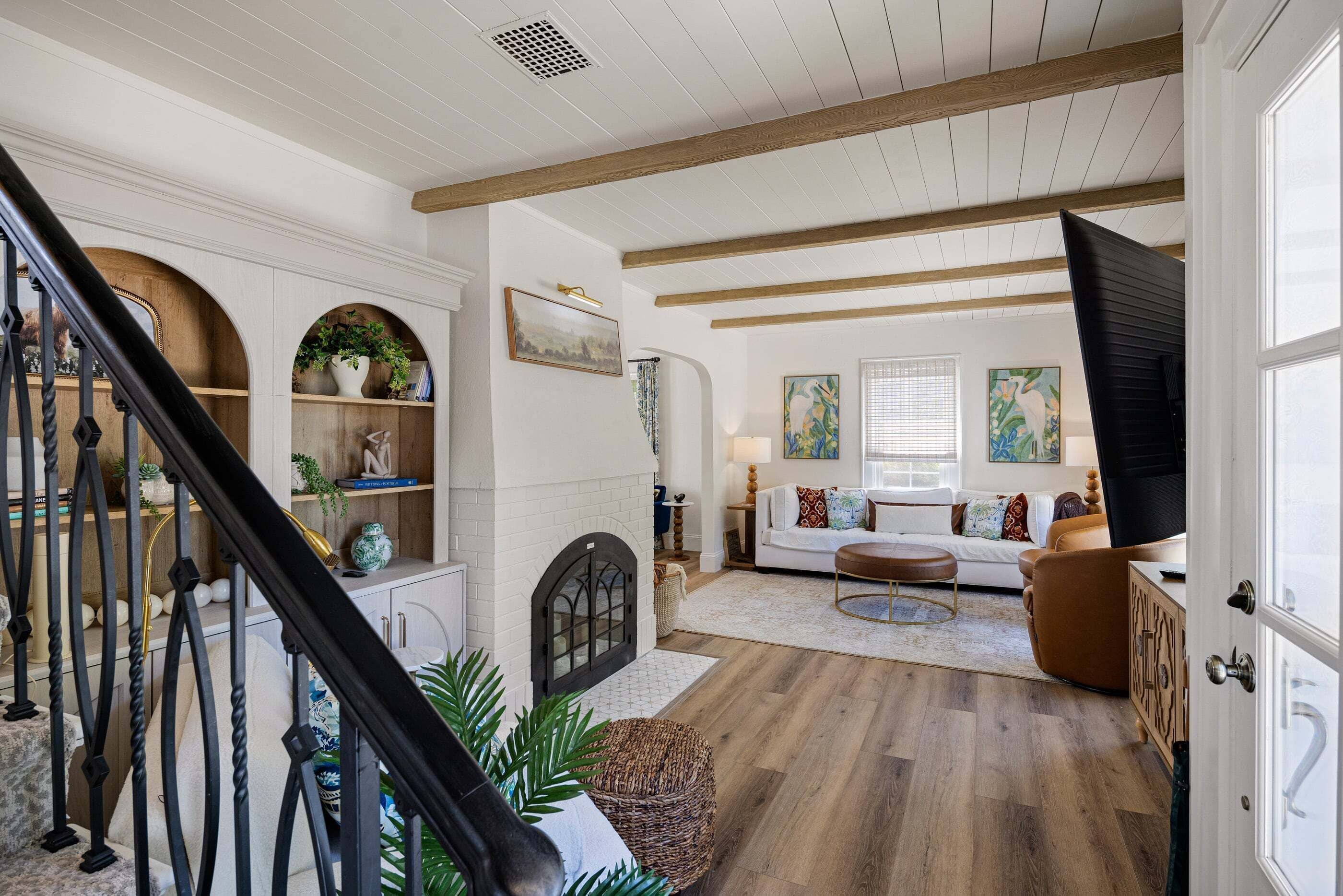 A spacious living area with a staircase, white walls, wooden beams, a fireplace, and a sofa set.