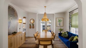 A dining area with a wooden table and chairs, a chandelier, and a blue sofa with cushions. - Bella Azul - Charming Home Minutes from Campus (Eugene)