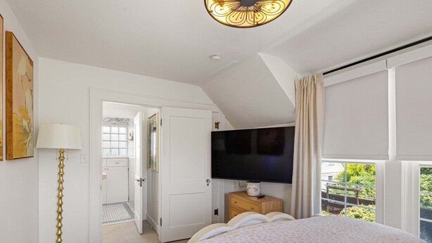 A bedroom with a bed, a television, a bedside table, a lamp, and a window with curtains. - Bella Azul - Charming Home Minutes from Campus (Eugene)