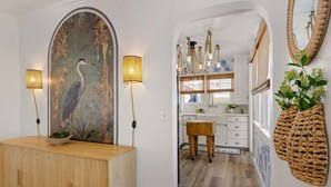 A hallway with a wooden cabinet, a wall-mounted lamp, and a large painting of a bird. - Bella Azul - Charming Home Minutes from Campus (Eugene)