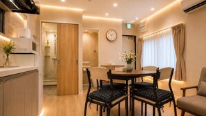 A modern hotel room with a dining area, a wooden door, a clock, and a vase with flowers.