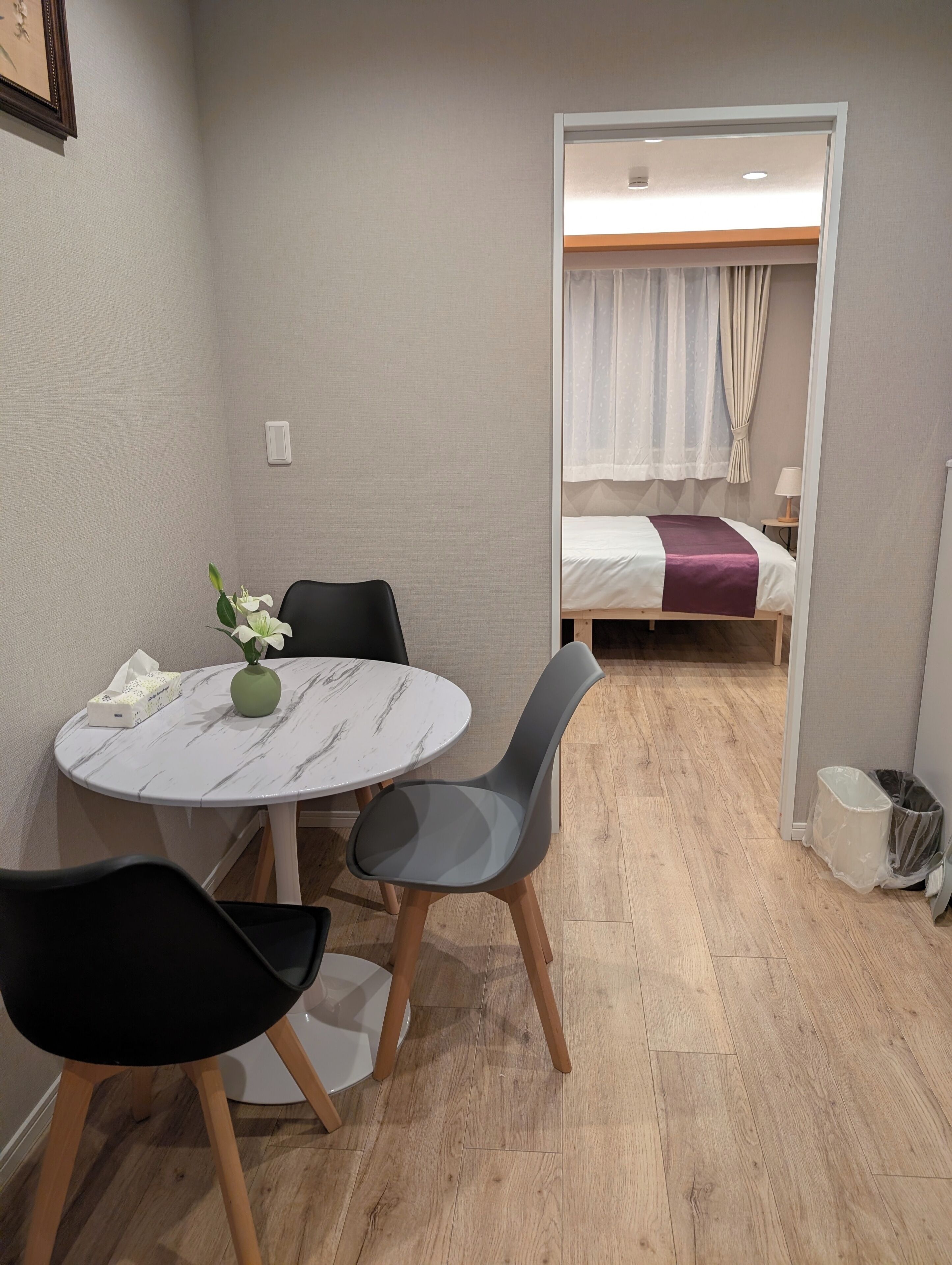 A small room with a round table, two chairs, a bed with a curtain, and a nightstand with a lamp.