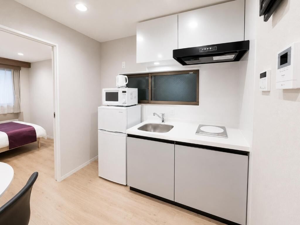 A compact kitchen with a microwave, sink, and stove, adjacent to a bed and a small table.