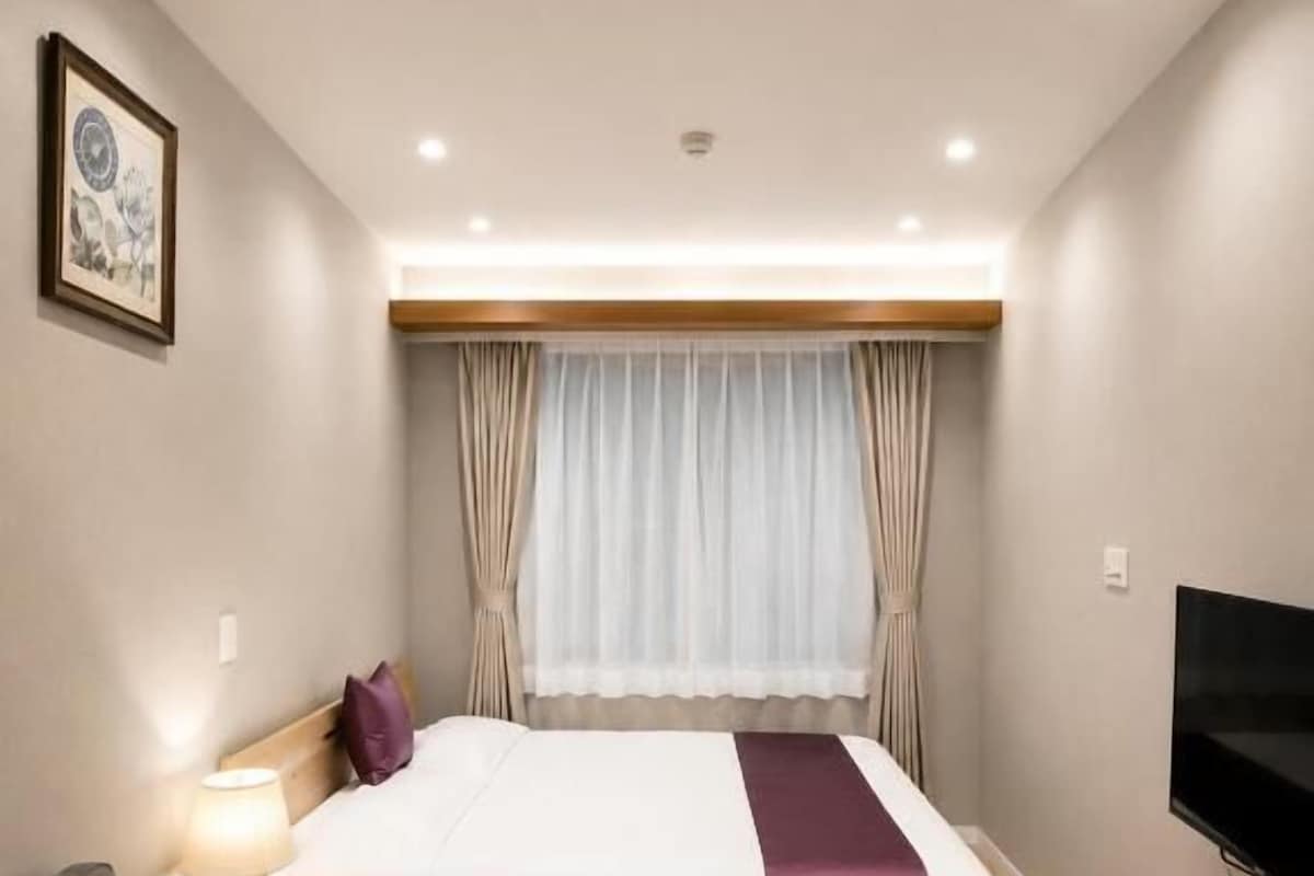 A hotel room with a bed, a sofa, a TV, and a window with curtains.