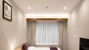 A hotel room with a bed, a sofa, a TV, and a window with curtains.