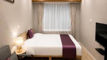 Una habitación de hotel con cama, sofá, televisor y ventana con cortinas.