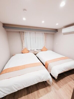 A room with two beds, a window with curtains, an air conditioning unit, and a ceiling light. - Star Minami-Senju (Taito-ku)