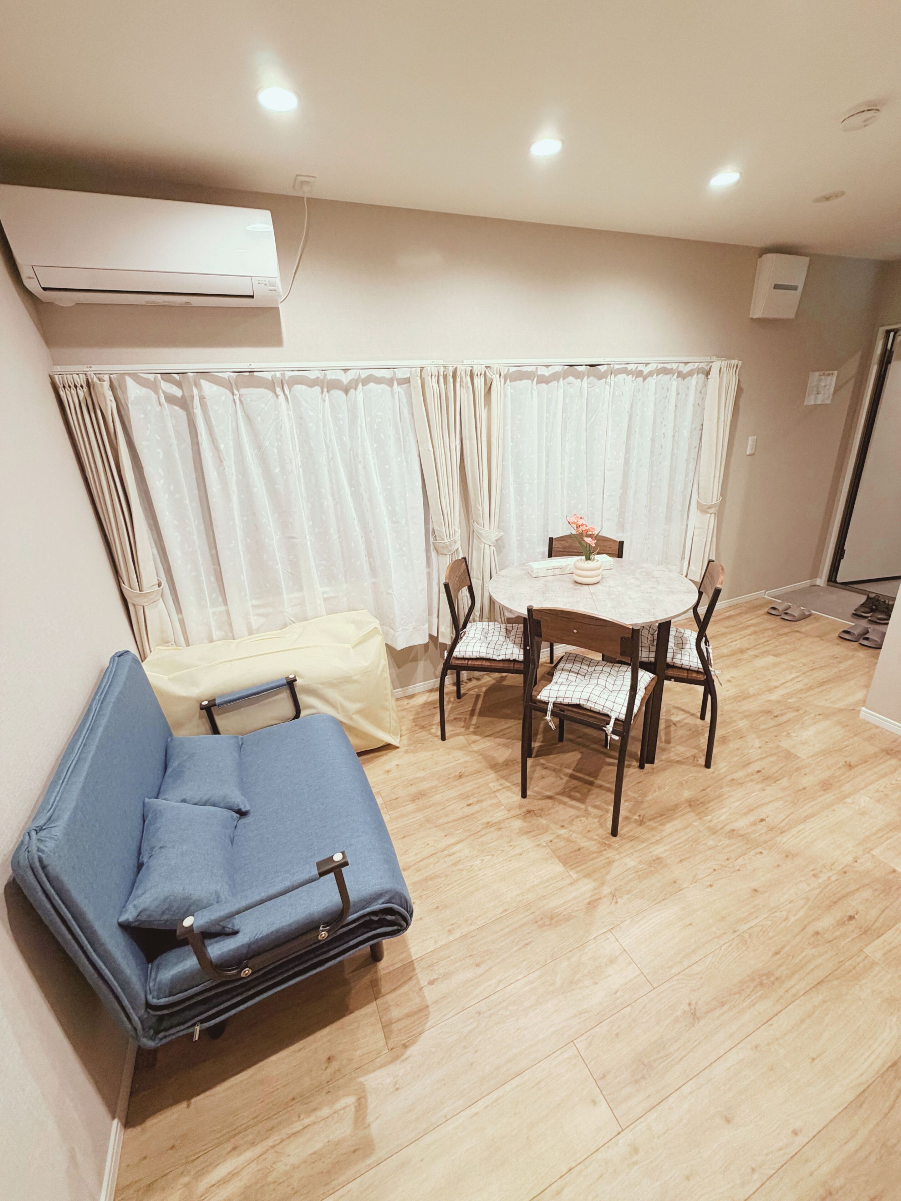A room with a bed, a table with chairs, a curtain, and an air conditioning unit.