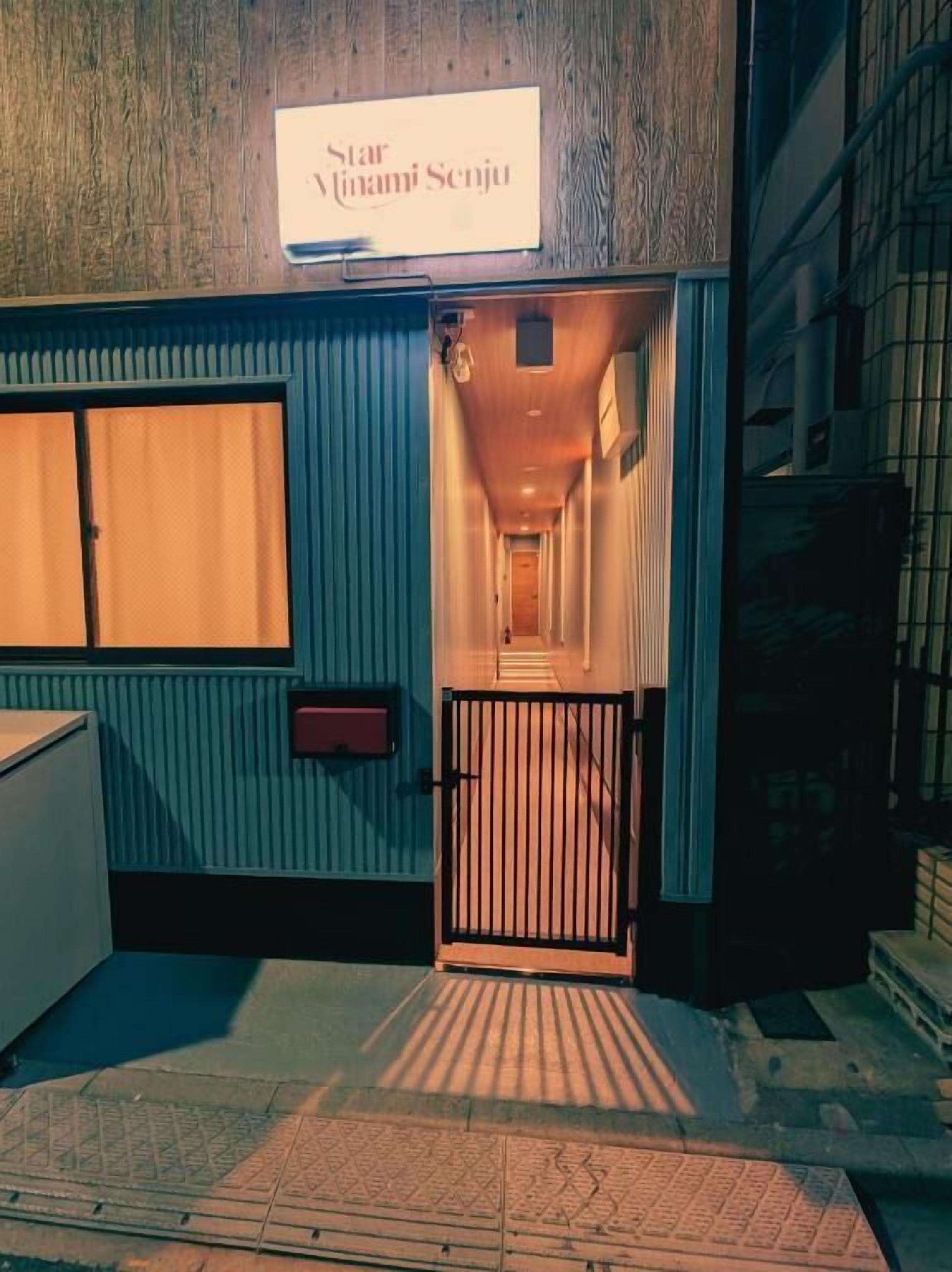 Entrada de un hotel con un cartel que dice 'Star Minami Senju', una puerta metálica y un estrecho pasillo que conduce al interior.