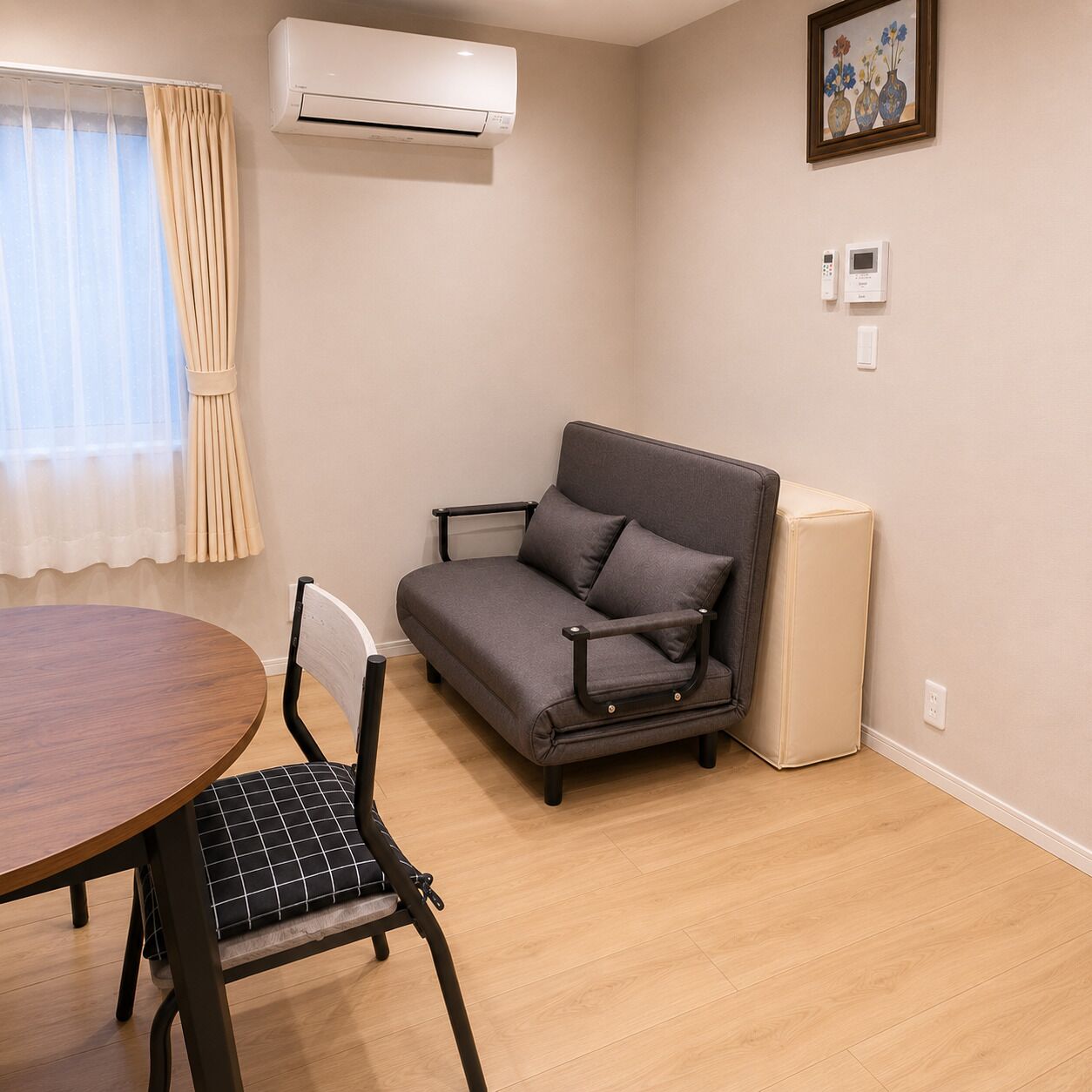 A room with a sofa, a dining table, a chair, an air conditioner, and a picture on the wall.