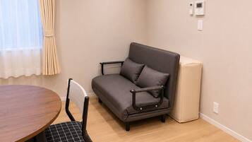 A room with a sofa, a dining table, a chair, an air conditioner, and a picture on the wall.