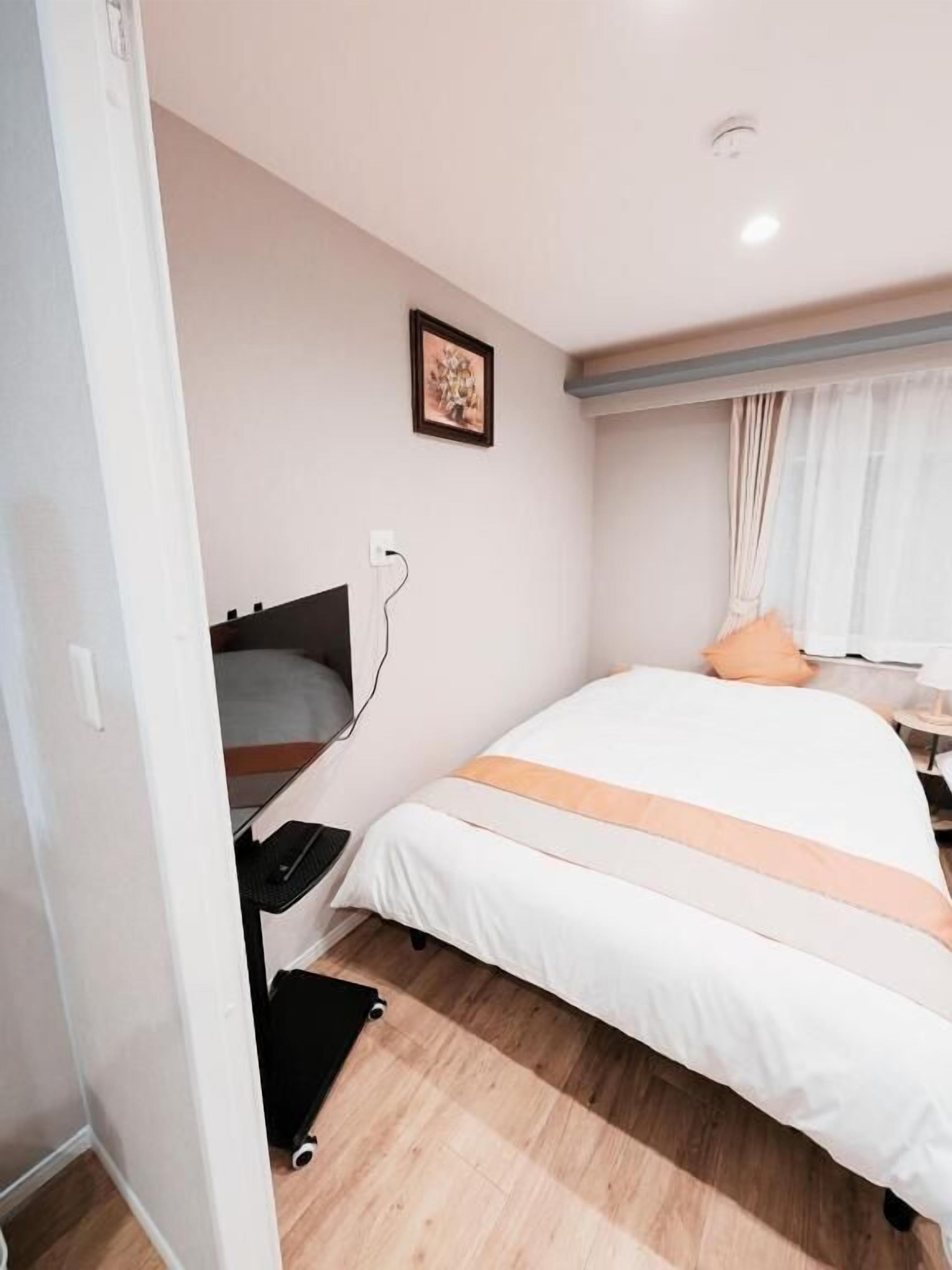A bedroom with a bed, a bedside table, a wall-mounted TV, and a window with curtains.