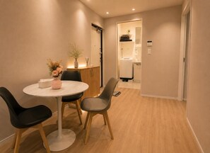 A modern hotel room with a round dining table, two chairs, a small vase with flowers, a cabinet, and a bathroom visible through an open door. - Star Minami-Senju (Taito-ku)