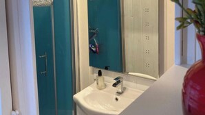 Een badkamer met een wit wastafelmeubel, een spiegel en een douchecabine.